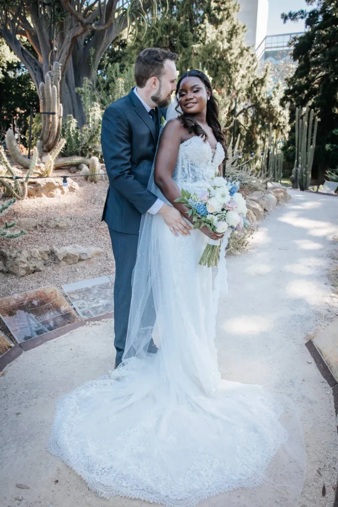 Bride and groom on a sunlit garden path, bride holding her bouquet